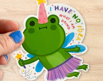 May include: A green frog wearing a pink party hat and a purple skirt with blue fairy wings. The frog is holding a magic wand and has a thought bubble above its head that says "I have no idea what I am doing".