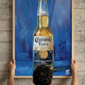 Puede incluir: Una pintura al óleo enmarcada que presenta una botella de cerveza Corona Extra de vidrio transparente centrada sobre un fondo azul profundo texturizado. La etiqueta muestra el texto Corona Extra, La Cerveza Mas Fina y Cerveceria Modelo S. de R.L. de C.V. Mexico.