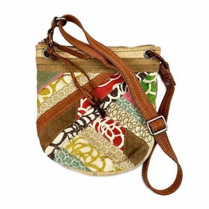 May include: A crossbody bag featuring a patchwork design of various fabrics in red, green, yellow, and white with brown suede accents. The bag includes a brown leather adjustable shoulder strap, a top zipper closure, and silver-toned metal hardware.
