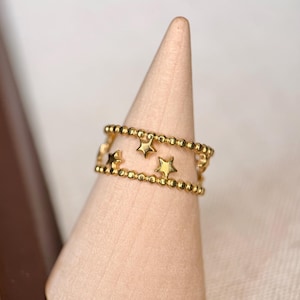 May include: A gold-toned ring featuring two parallel bands of small, uniform beads. Between the beaded bands, several small, five-pointed star shapes are evenly spaced, creating a delicate and open design that encircles the finger.