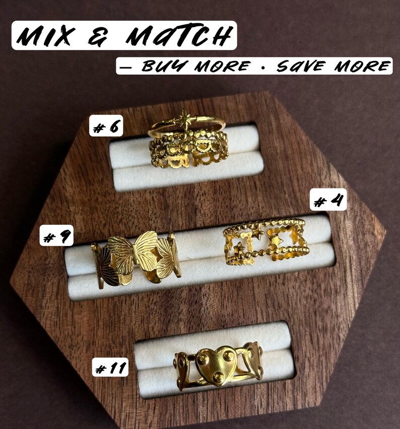 May include: Four gold-toned rings displayed on a wooden holder. Ring #6 features a star and scalloped band. Ring #9 has a butterfly motif. Ring #4 displays a star pattern. Ring #11 shows a heart design. Text reads MIX & MATCH - BUY MORE - SAVE MORE.