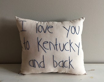 May include: A white pillow with blue embroidery that reads "I love you to Kentucky and back".