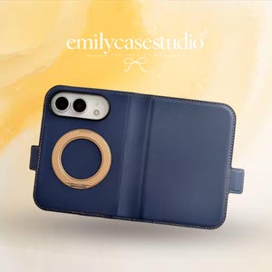 Può includere: Una custodia per telefono blu navy a portafoglio con un anello magnetico circolare dorato sul retro, un ritaglio per la fotocamera e una linguetta laterale. Il testo emilycasestudio è visibile sopra la custodia su uno sfondo giallo.