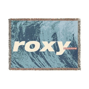 May include: A rectangular woven throw blanket featuring a large, crashing ocean wave in shades of dark blue and light teal. The word "roxy" is printed in large, cream-colored letters across the center, with a small red logo tag on the right.
