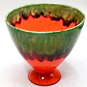 May include: A small, orange and green ceramic bowl with a flared rim and a footed base. The bowl has a mottled glaze with shades of green, brown, and orange.