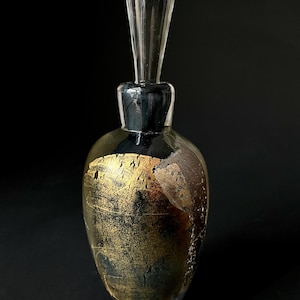 May include: A clear glass bottle with a gold and black design. The bottle has a clear glass stopper.