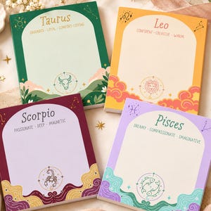 May include: Four rectangular paper notepads featuring zodiac signs Taurus, Leo, Scorpio, and Pisces. Each notepad displays the sign name, descriptive traits, and a central circular icon with a corresponding illustration and decorative border elements.