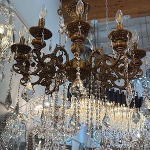 May include: A multi-tiered antique brass chandelier featuring ornate scrollwork arms, six upward-facing candle-style light sockets, and numerous clear glass crystal teardrop pendants hanging from the frame, suspended by a central metal chain.