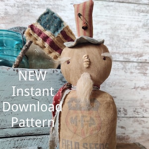 May include: A handmade rag doll dressed in a burlap sack with a red, white and blue scarf and a striped hat. The doll has a white beard and a painted face. The sack has the words "M.F. Field Seeds 1776" printed on it.