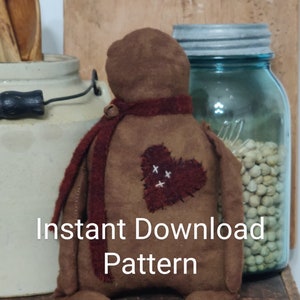 May include: A brown felt doll with a red felt scarf and a heart-shaped patch on its chest. The doll is sitting on a wooden box with the word "GSFORD'S" printed on it. The text "Instant Download Pattern" is printed on the image.