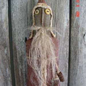 May include: A handmade rag doll Santa Claus with a long white beard, brown felt body, and a white felt hat. The doll has button eyes and is decorated with pine cones.