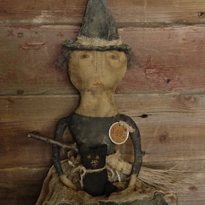 May include: A handmade rag doll witch wearing a black pointed hat with a brown brim and a black dress. She is holding a black cat and a broom. The doll has a brown tag with the number 1692 on it.