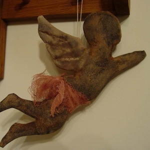 May include: A brown fabric angel ornament with a pink tulle skirt and wings. The angel is hanging from a white string.