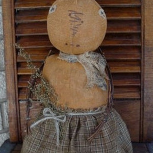 May include: A handmade rag doll with a brown and tan plaid skirt, a brown burlap head, and a brown twig body. The doll is holding a small bouquet of dried flowers.