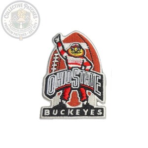 Puede incluir: Un parche bordado que presenta a la mascota de los Ohio State Buckeyes, Brutus, en rojo, blanco y negro. La mascota está colocada frente a una forma de balón de fútbol americano con el texto OHIO STATE en negrita y BUCKEYES en la parte inferior.