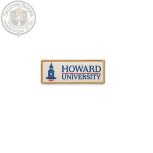 Puede incluir: Un parche rectangular bordado con fondo color crema y borde dorado. Presenta un gráfico azul de una torre de reloj, el texto "HOWARD UNIVERSITY" en azul y el año "1867" en rojo, todo centrado sobre la superficie de la tela.