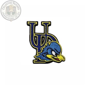 May include: An embroidered patch featuring the letters UD in dark blue with a yellow border, layered behind a blue bird mascot head with a yellow beak, white eye, and red mouth detail, all outlined in black thread against a white background.