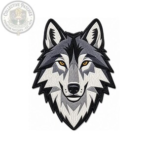 Könnte beinhalten: Ein gestickter Aufnäher mit einem stilisierten Wolfskopf mit geometrischen Mustern in Grau-, Weiß- und Schwarztönen. Der Wolf hat stechende bernsteinfarbene Augen und eine schwarze Nase, umrandet von einem dicken schwarzen Rand.