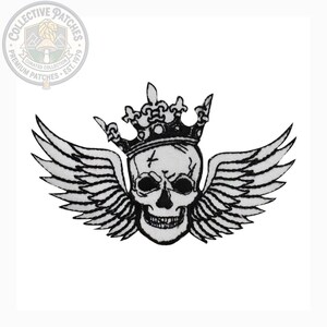 May include: An embroidered patch featuring a white skull with black outlines, wearing a black and white crown with fleur-de-lis details. The skull is flanked by two large, detailed white wings with black outlines, creating a symmetrical design.