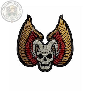 May include: An embroidered patch featuring a central white skull with curved horns, flanked by two large wings. The wings are detailed with gold and red thread, and the entire design is outlined in black, creating a bold, high-contrast graphic.