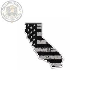 Puede incluir: Un parche de tela con la forma del estado de California que presenta un diseño de bandera estadounidense en blanco y negro con efecto desgastado. El parche muestra un campo de estrellas blancas a la izquierda y rayas horizontales texturizadas.