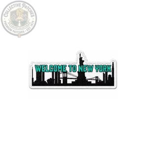 May include: A rectangular embroidered patch featuring a black silhouette of the New York City skyline, including the Statue of Liberty and a bridge. The text WELCOME TO NEW YORK is embroidered in bright teal letters across the center of the patch.