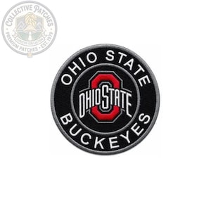 May include: A circular embroidered patch featuring a black background with a grey border. The text OHIO STATE BUCKEYES is stitched in white around the center. A red and white block O logo with the word OHIO STATE is centered in the middle.