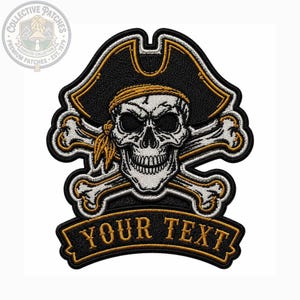Puede incluir: Un parche bordado que muestra una calavera blanca con un sombrero de pirata negro y dorado y un pañuelo a juego. Detrás de la calavera hay dos huesos blancos cruzados con bordes dorados. Debajo, una cinta negra lleva el texto YOUR TEXT.