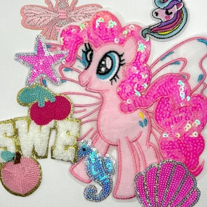 May include: A collection of embroidered patches featuring a pink pony with sequins, a pink butterfly, a unicorn head, a pink star, a pair of cherries, a peach, the letters SWE, a blue seahorse, and a pink seashell with silver glitter accents.