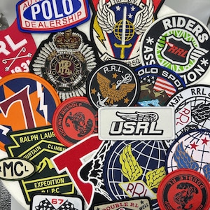 Puede incluir: Una colección de parches de tela bordados con varios diseños, incluyendo los textos Authorized Polo Dealership, 118th Div, Riders Association, USRL, Ralph Lauren, Ridgway Roundup, Double RL y varios emblemas gráficos como águilas, espadas y banderas.