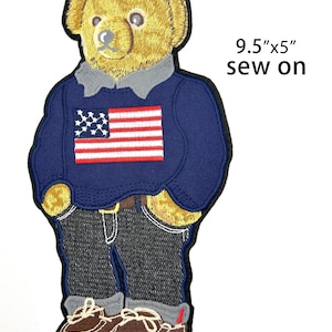 May include: An embroidered sew-on patch measuring 9.5 inches by 5 inches, featuring a golden-brown teddy bear wearing a navy blue sweater with an American flag design, dark gray jeans with rolled cuffs, and brown boat shoes, labeled with the number 04.