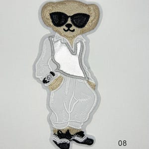 May include: An embroidered patch featuring a tan bear wearing black sunglasses, a white collared shirt, and light grey trousers. The bear has a black wristwatch on its left arm and black shoes. Text on the image reads 08 21.6 cm x 9.7 cm Sew on.