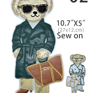 May include: An embroidered sew-on patch featuring a bear wearing sunglasses, a dark green trench coat, and tan trousers, holding a brown handbag. The patch measures 10.7 inches by 5 inches. The text 02 and rverse side are visible in the image.