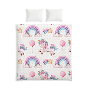 May include: A white duvet cover and two matching pillowcases featuring a repeating pattern of unicorns with pink and teal manes, colorful rainbows, pink balloons, and yellow stars against a background of small, light pink polka dots.