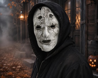 May include: A white, cracked, weathered mask with dark eye sockets and deep fissures across the surface, worn under a black hooded jacket. The mask features a textured, aged appearance with dark streaks and a neutral, hollow facial expression.