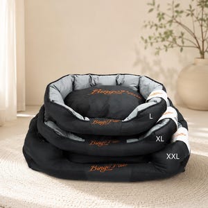 Puede incluir: Tres camas para mascotas apiladas en tallas L, XL y XXL. Cada cama es negra con un forro interior gris claro y presenta el texto BingoPaw bordado en naranja en la parte frontal. Las camas tienen bordes elevados y un cojín central suave.