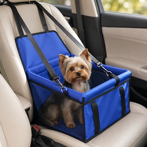 Puede incluir: Un asiento elevador para mascotas de color azul con bordes negros y paneles laterales de malla, asegurado con correas negras ajustables. Un pequeño Yorkshire Terrier de pelaje marrón y negro está sentado dentro del transportín rectangular.