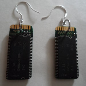 May include: A pair of unique earrings made from recycled computer components. Each earring features a rectangular black circuit board with gold-colored contacts and silver-colored ear wires. The earrings are a creative blend of technology and fashion.