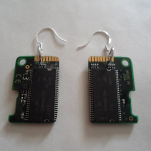 May include: A pair of unique earrings made from repurposed circuit board components. Each earring features a rectangular green circuit board with silver-tone ear wires. The boards have gold-colored connectors and black integrated circuits.