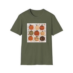 May include: An olive green short-sleeved t-shirt featuring a square graphic print on the chest. The print displays nine pumpkins in various shades of orange, brown, and cream, decorated with patterns like diamonds, moons, and leaves on a white background.