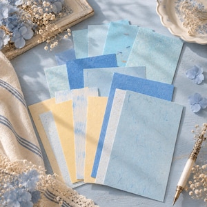 May include: A collection of rectangular paper sheets in various shades of blue and pale yellow, featuring textured surfaces with visible fibers. The papers are arranged in a fan-like stack, displaying different tones ranging from light sky blue to deep azure.