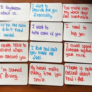 Puede incluir: Doce tarjetas rectangulares blancas dispuestas en una cuadrícula, cada una con texto escrito a mano en tinta roja, azul o morada. Los mensajes incluyen frases como I daydream about us, I want to provide for you financially y You make even my worst days feel survivable.