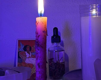 May include: A lit taper candle with a textured surface stands before a clear glass dropper bottle containing botanical elements, a tarot card featuring a seated figure, and a large white pillar candle, all illuminated by purple light.