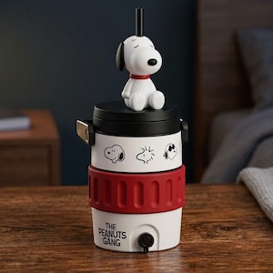Może przedstawiać: Biało-czarny chłodziarka do napojów z figurką Snoopy'ego na pokrywce, czerwonym silikonowym paskiem i czarnym kranikiem. Korpus ozdobiony jest czarnymi rysunkami postaci z Peanuts oraz czarnym napisem THE PEANUTS GANG na przedniej stronie.