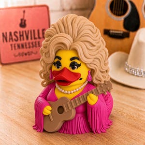 Puede incluir: Una figura de pato de goma amarillo con cabello rubio voluminoso, vistiendo un vestido rosa brillante con flecos, un collar de perlas y pendientes rosas. El pato sostiene una pequeña guitarra acústica marrón, tiene un pico rojo y pestañas negras.