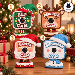 May include: Four decorative holiday cameras labelled Elf Cam, Reindeer Cam, Santa Cam, and Snowman Cam. Each camera features a character-themed design with a central lens, festive hats, and colours including green, brown, red, and blue.