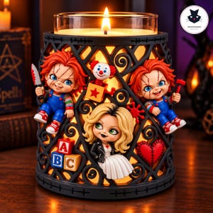 Puede incluir: Un calentador de velas decorativo negro con diseño de celosía, adornado con dos muñecos pelirrojos con peto azul, uno con un cuchillo y otro con un martillo, una muñeca rubia con vestido blanco, una caja sorpresa, bloques de letras y un corazón rojo.