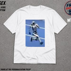 May include: A white short-sleeved t-shirt featuring a central rectangular graphic of a blurred figure in motion against a blue background. The shirt includes text elements reading UNISEX, ADULTS & KIDS, 100% COTTON, FREE SHIPPING US, and WHITE.