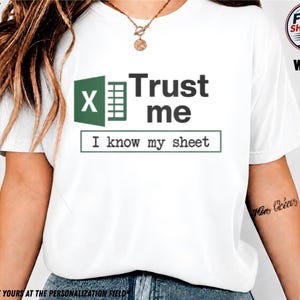 Könnte beinhalten: Ein weißes T-Shirt mit einem grün-weißen Tabellenkalkulations-Symbol neben dem dunkelgrauen Text "Trust me" und einem rechteckigen Kasten mit dem Text "I know my sheet" in einer Schreibmaschinen-Schriftart auf der Brust des Kleidungsstücks.