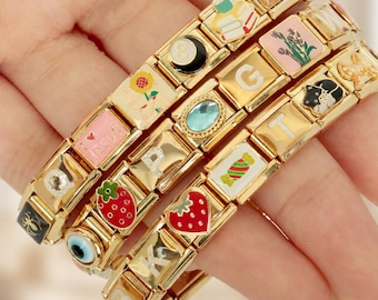 Op de afbeelding: Drie goudkleurige modulaire schakelarmbanden met diverse emaille bedels, waaronder een aardbei, zonnebloem, kat, snoepje, blauw oog, bloemenboeket, stapel boeken en de letters G, T, K, B, P en de tekst I LOVE JESUS.